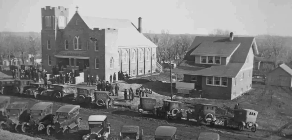 A historic black and white photo of Immanuel Lutheran Church and surrounding buildings with cars and people.